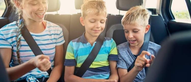 A group of kids laughing and playing rock, paper, scissors in a car during a road trip