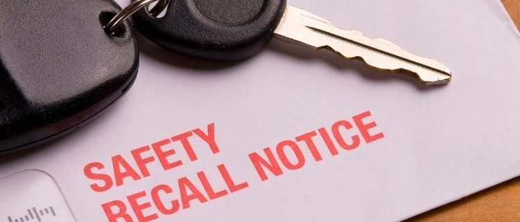 Vehicle safety recall notice in an envelope placed on a desk beside a set of car keys, symbolizing the importance of addressing automotive safety issues.