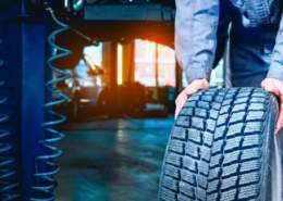 A mechanic rotating car tires in a garage, emphasizing the importance of regular tire rotations.