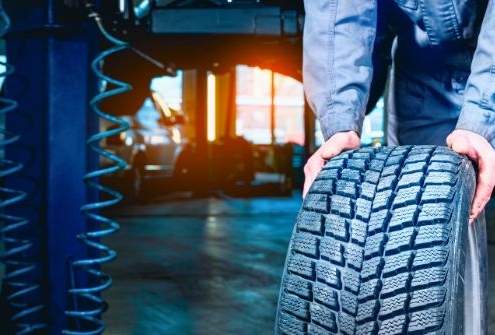 A mechanic rotating car tires in a garage, emphasizing the importance of regular tire rotations.